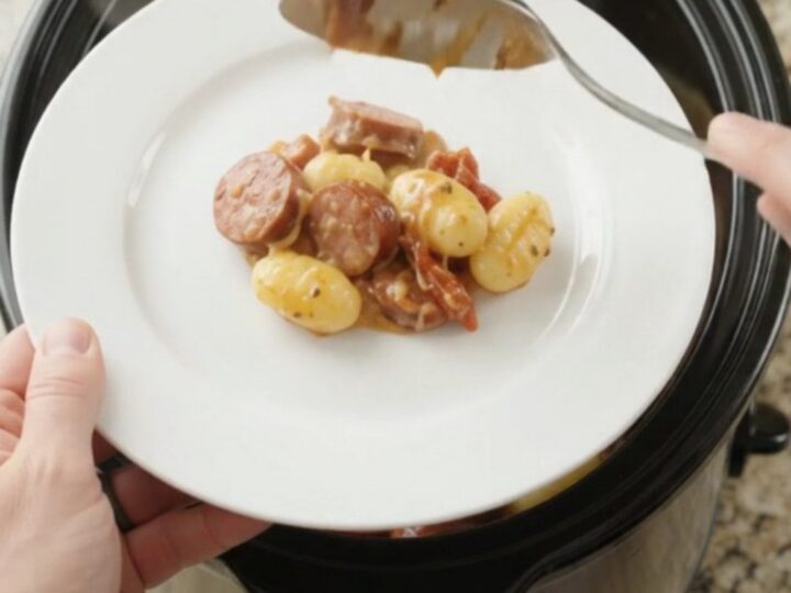 Slow cooker filled with creamy kielbasa Tuscan gnocchi, topped with melted provolone and ricotta