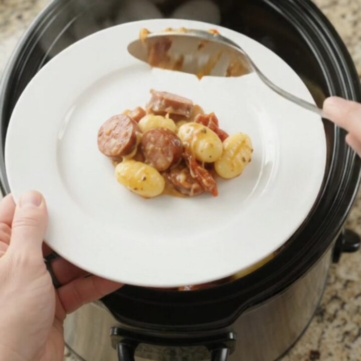 Slow cooker filled with creamy kielbasa Tuscan gnocchi, topped with melted provolone and ricotta