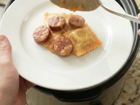 Slow cooker filled with creamy kielbasa vodka ravioli, topped with melted fontina and Boursin cheese.