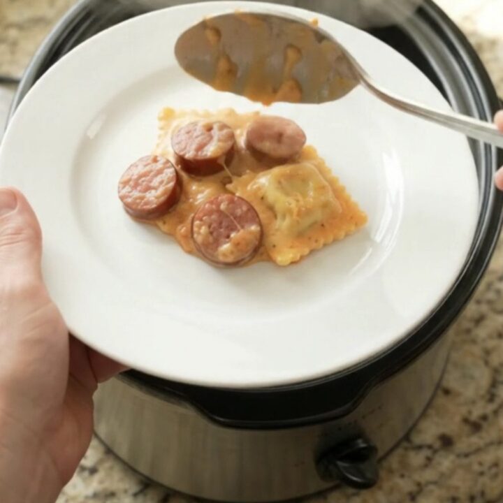 Slow cooker filled with creamy kielbasa vodka ravioli, topped with melted fontina and Boursin cheese.