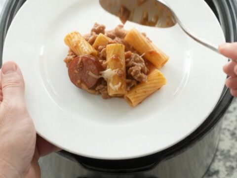 Slow cooker full of cheesy rigatoni with kielbasa and tomato sauce, golden crust on top.