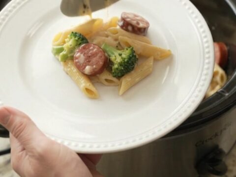 Slow cooker filled with creamy kielbasa Alfredo penne, garnished with parsley.