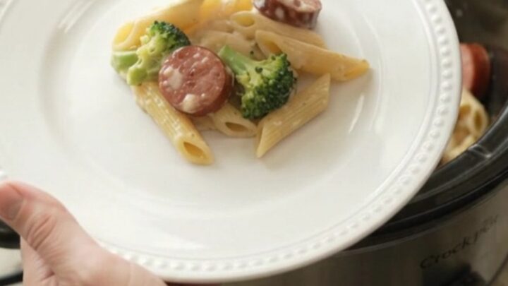 Slow cooker filled with creamy kielbasa Alfredo penne, garnished with parsley.