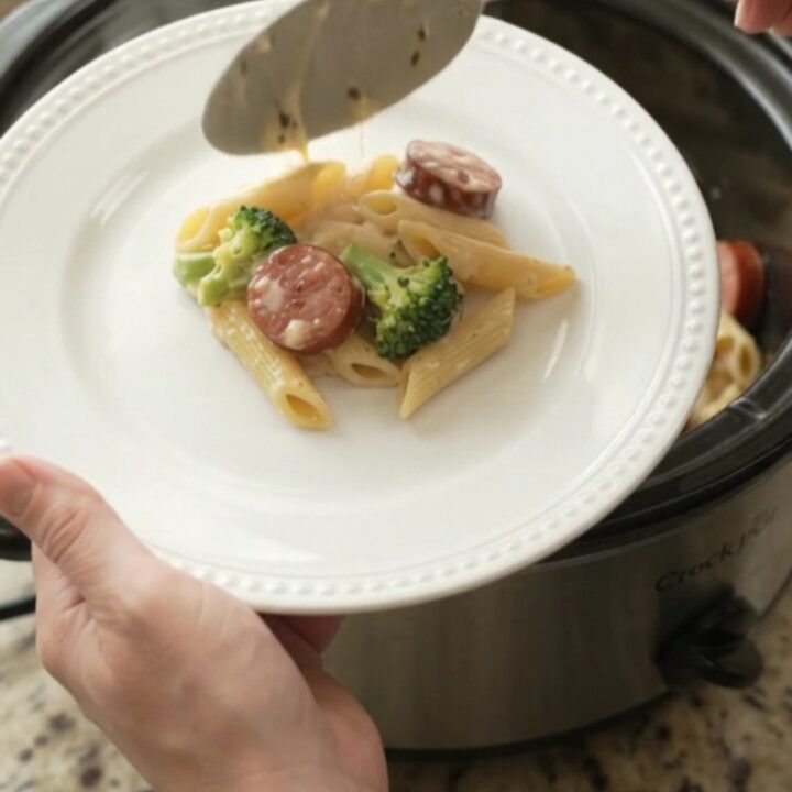 Slow cooker filled with creamy kielbasa Alfredo penne, garnished with parsley.