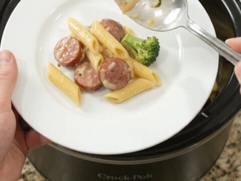 Slow cooker filled with creamy kielbasa Alfredo penne topped with melted cheese and broccoli