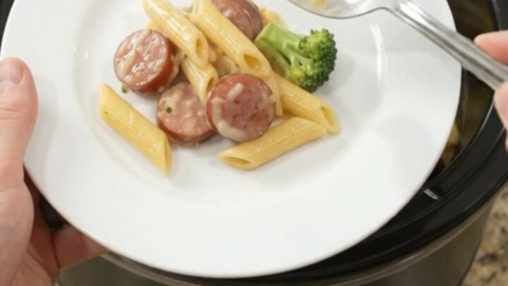 Slow cooker filled with creamy kielbasa Alfredo penne topped with melted cheese and broccoli