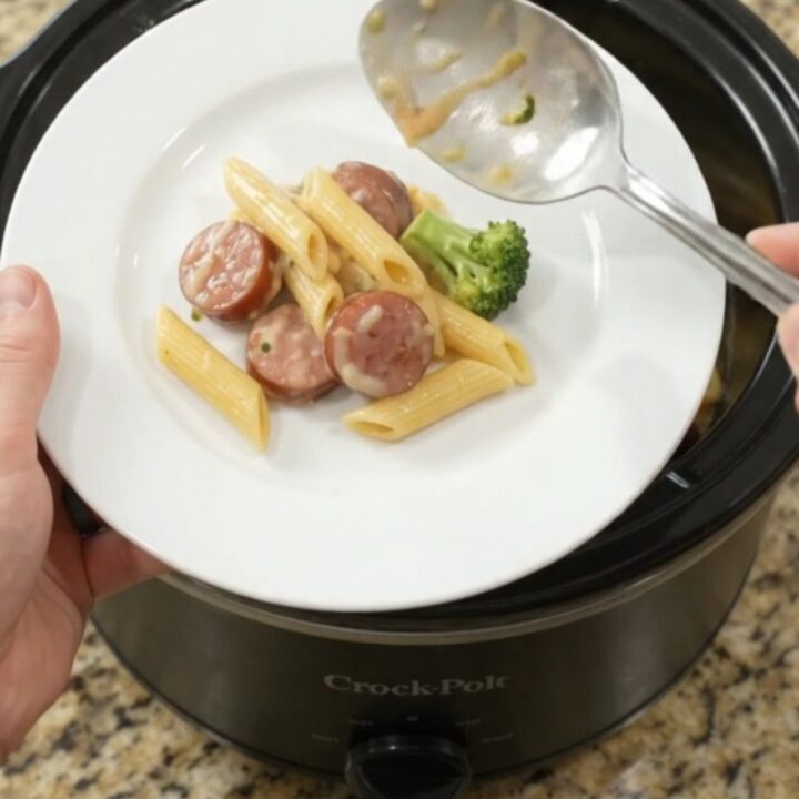 Slow cooker filled with creamy kielbasa Alfredo penne topped with melted cheese and broccoli