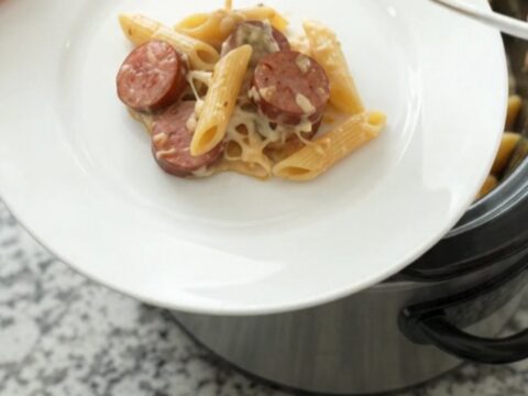 Slow cooker filled with creamy Alfredo penne, kielbasa, and broccoli topped with melted provolone.