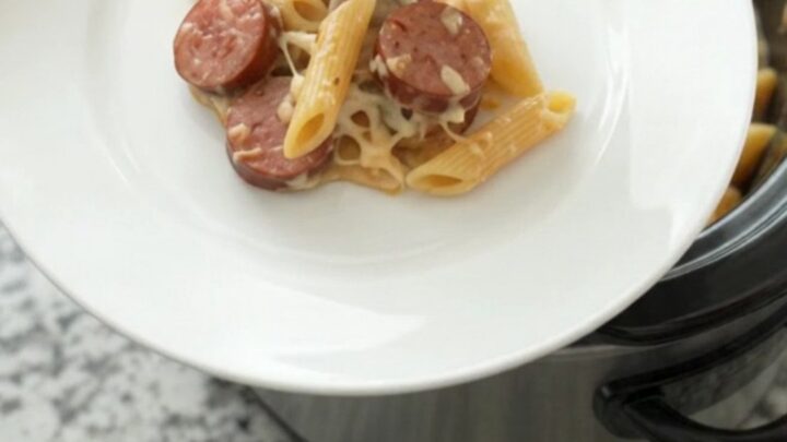 Slow cooker filled with creamy Alfredo penne, kielbasa, and broccoli topped with melted provolone.