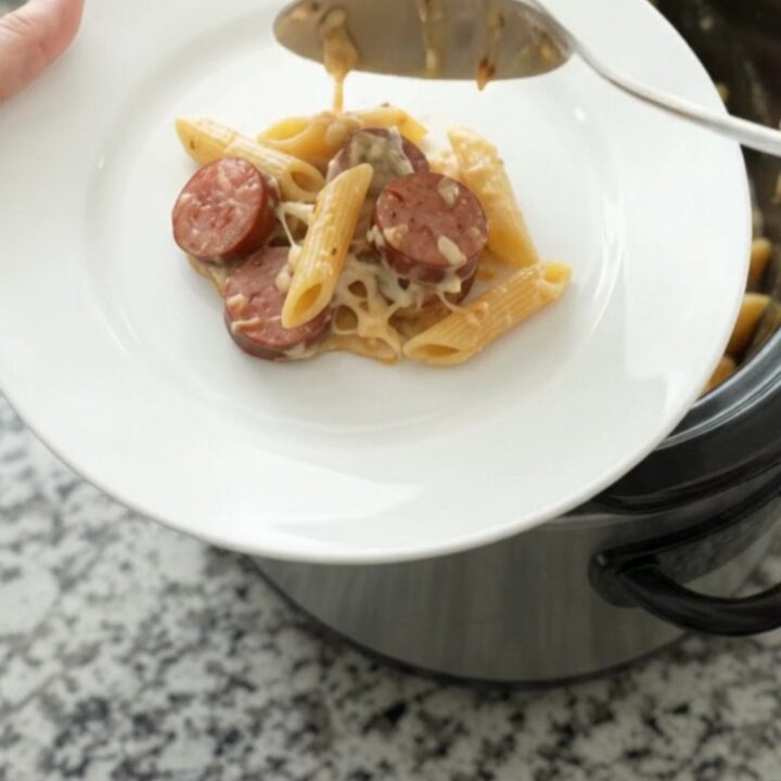 Slow cooker filled with creamy Alfredo penne, kielbasa, and broccoli topped with melted provolone.