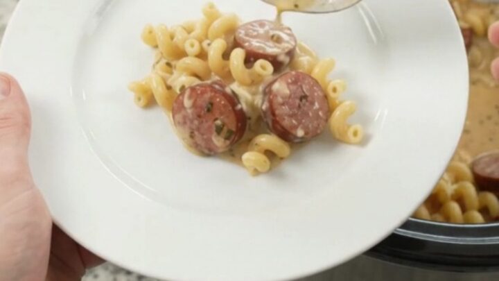 Slow cooker filled with creamy cavatappi pasta and kielbasa, topped with melted cheese