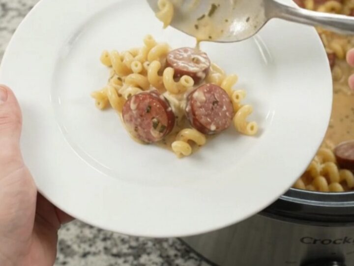 Slow cooker filled with creamy cavatappi pasta and kielbasa, topped with melted cheese