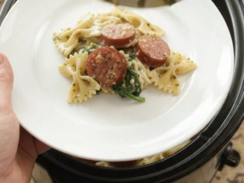Crockpot full of creamy pesto farfalle with smoked kielbasa, melted mozzarella, and wilted spinach