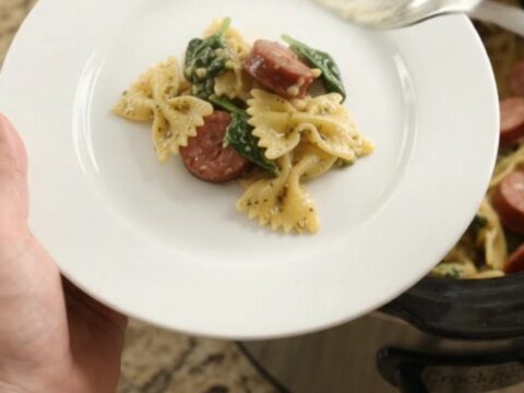Slow cooker filled with bubbling cheesy pasta, kielbasa, and spinach, topped with melted Parmesan
