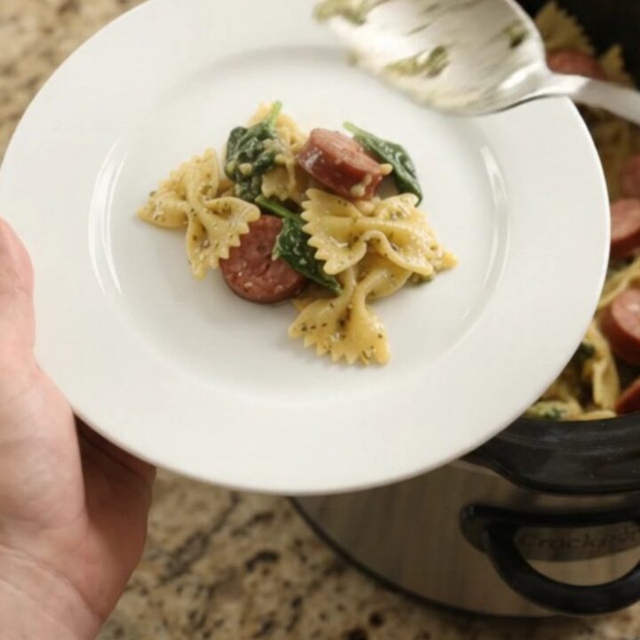 Slow cooker filled with bubbling cheesy pasta, kielbasa, and spinach, topped with melted Parmesan