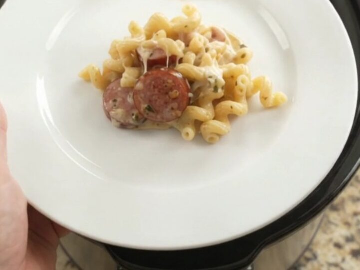 Slow cooker full of creamy cavatappi with kielbasa, melted cheese, and steam rising