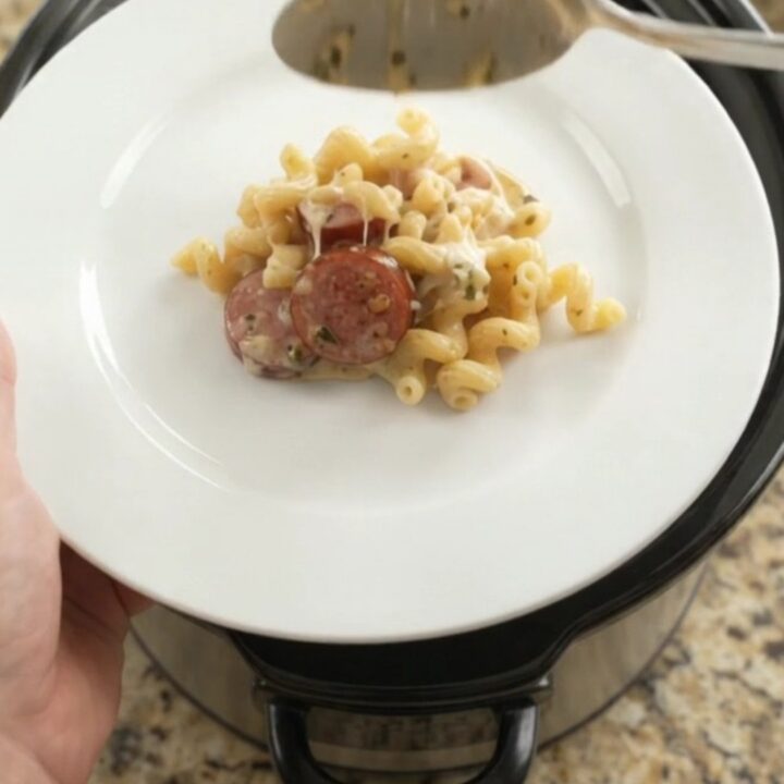 Slow cooker full of creamy cavatappi with kielbasa, melted cheese, and steam rising