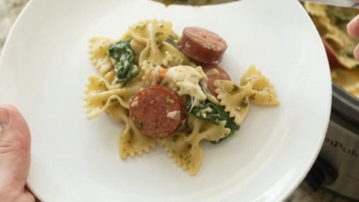 Crockpot full of creamy kielbasa pesto farfalle with melted provolone and spinach