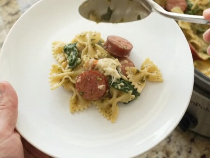 Crockpot full of creamy kielbasa pesto farfalle with melted provolone and spinach