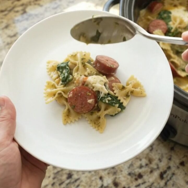 Crockpot full of creamy kielbasa pesto farfalle with melted provolone and spinach