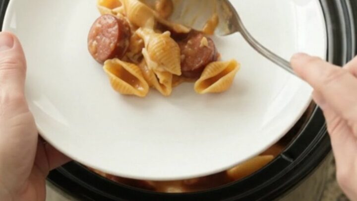 Slow cooker filled with creamy pasta shells, kielbasa, and melted cheese, topped with Boursin and fontina