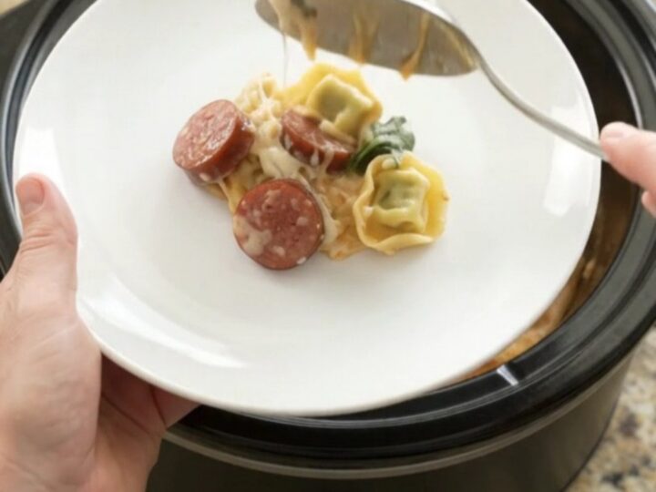 Slow cooker filled with creamy kielbasa tortellini Alfredo, with melted cheese and mushrooms visible