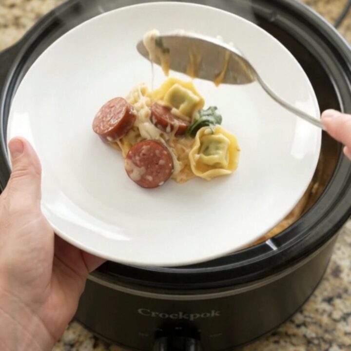 Slow cooker filled with creamy kielbasa tortellini Alfredo, with melted cheese and mushrooms visible