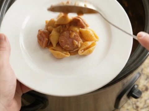 Slow cooker filled with cheesy pasta shells and smoked kielbasa, topped with melted cheese and Parmesan crust