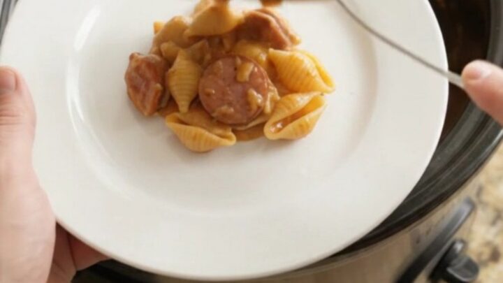 Slow cooker filled with cheesy pasta shells and smoked kielbasa, topped with melted cheese and Parmesan crust