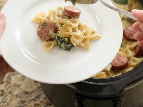 Creamy slow-cooker farfalle with smoked kielbasa, spinach, and melted cheese in a black crockpot