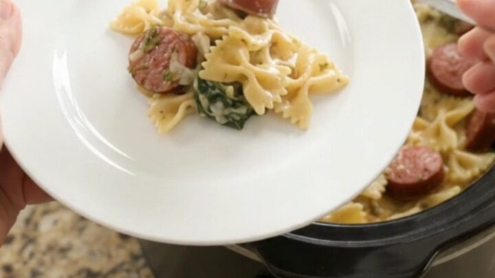 Creamy slow-cooker farfalle with smoked kielbasa, spinach, and melted cheese in a black crockpot