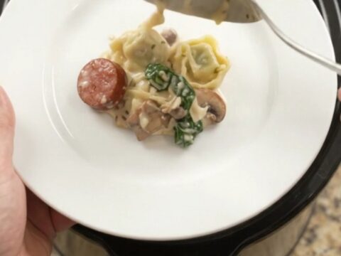 Bubbling slow cooker with creamy kielbasa and tortellini pasta bake, topped with melted fontina.
