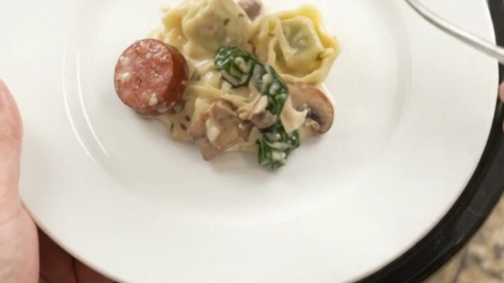 Bubbling slow cooker with creamy kielbasa and tortellini pasta bake, topped with melted fontina.