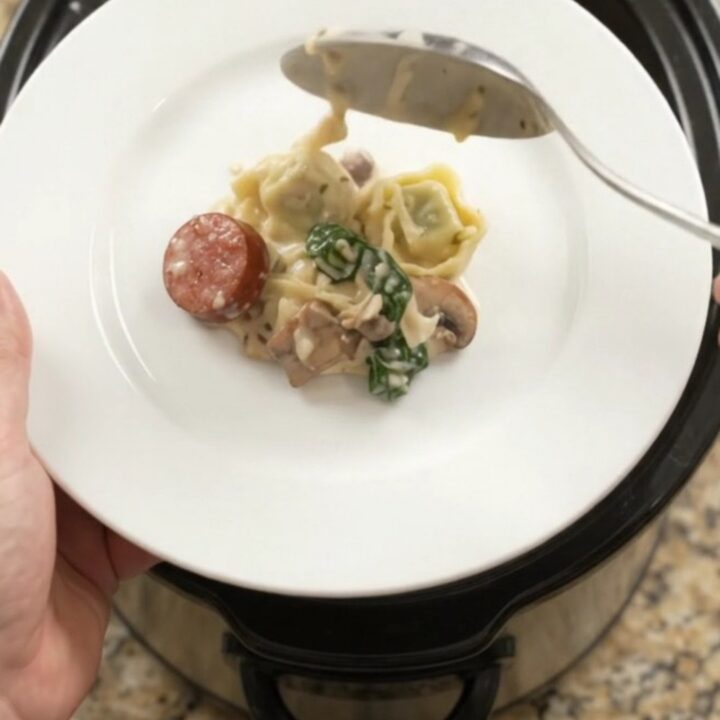 Bubbling slow cooker with creamy kielbasa and tortellini pasta bake, topped with melted fontina.