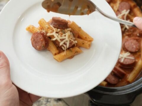 Slow cooker filled with bubbling kielbasa baked ziti, topped with melted mozzarella and steam rising