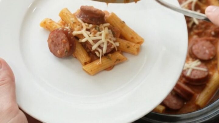 Slow cooker filled with bubbling kielbasa baked ziti, topped with melted mozzarella and steam rising