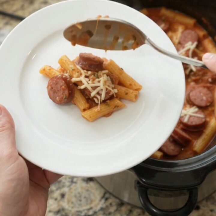 Slow cooker filled with bubbling kielbasa baked ziti, topped with melted mozzarella and steam rising
