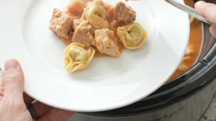 Slow cooker filled with creamy chicken tortellini in tomato sauce, topped with melted fontina