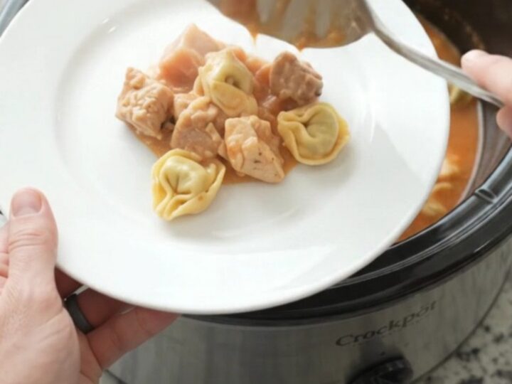 Slow cooker filled with creamy chicken tortellini in tomato sauce, topped with melted fontina