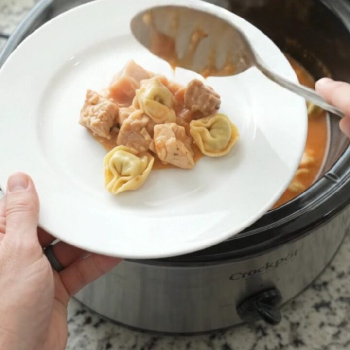 Slow cooker filled with creamy chicken tortellini in tomato sauce, topped with melted fontina
