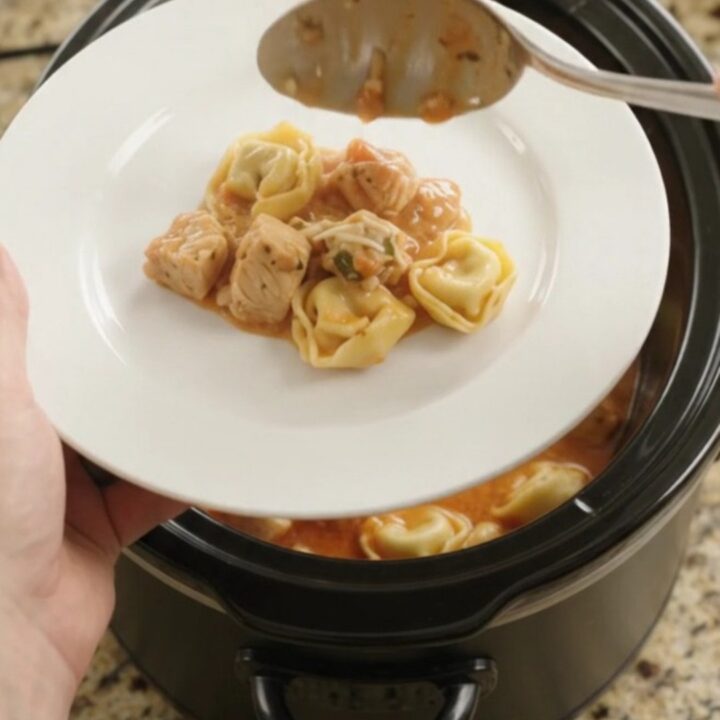 Slow cooker filled with bubbling chicken tortellini in creamy tomato sauce, topped with melted provolone.