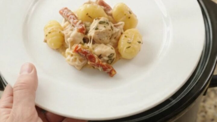 Crockpot Boursin chicken and gnocchi with creamy sauce, topped with melted fontina, in a black slow cooker.