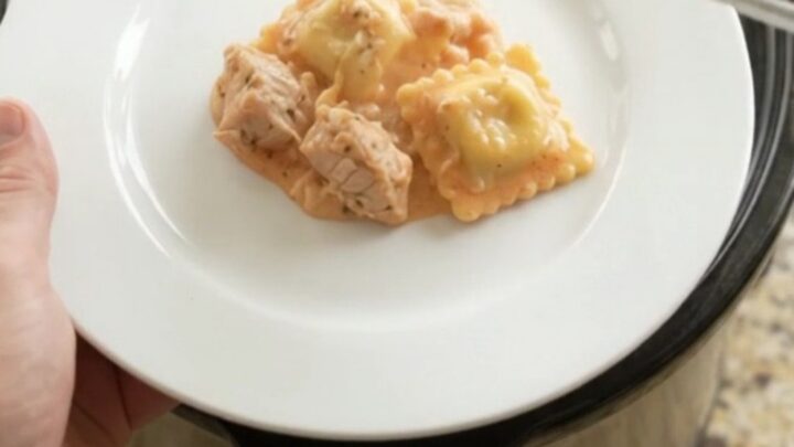 Slow cooker filled with cheesy chicken and ravioli in vodka sauce, golden crust on top