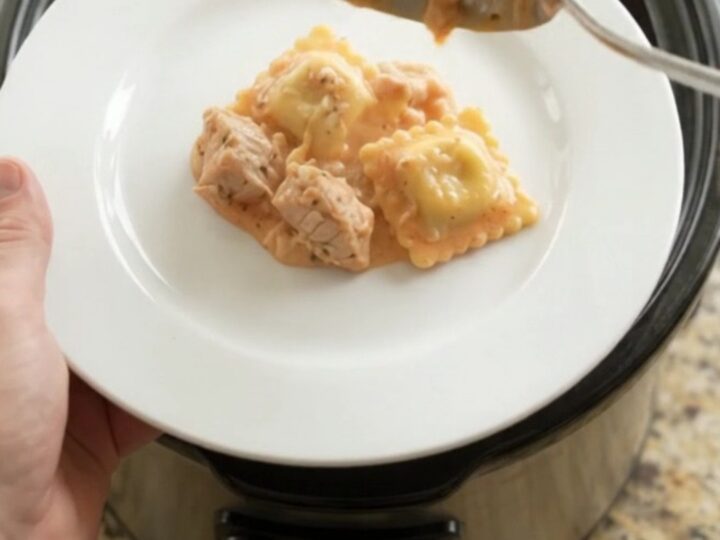 Slow cooker filled with cheesy chicken and ravioli in vodka sauce, golden crust on top