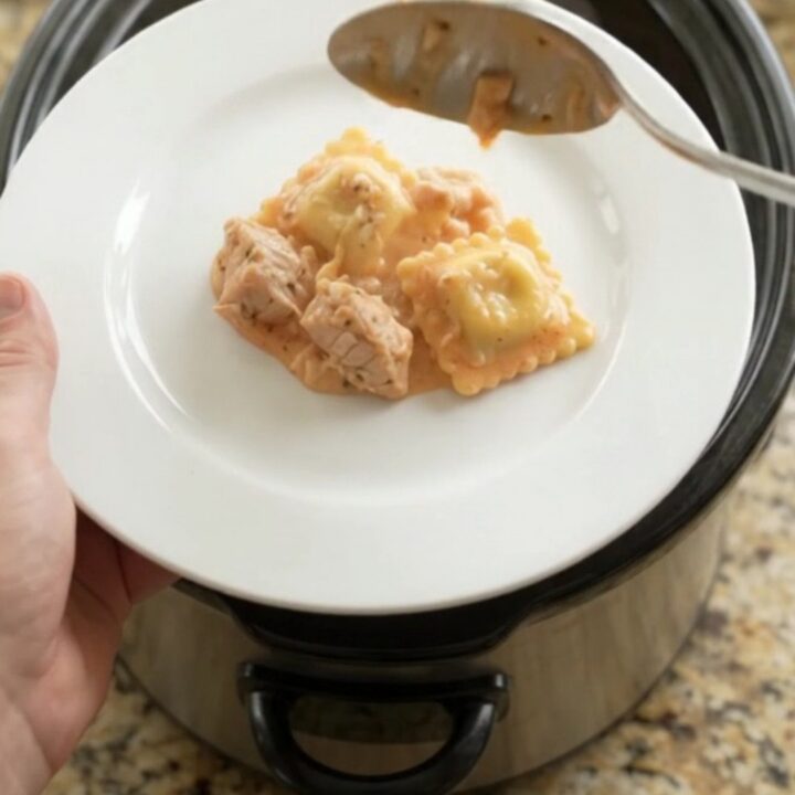 Slow cooker filled with cheesy chicken and ravioli in vodka sauce, golden crust on top