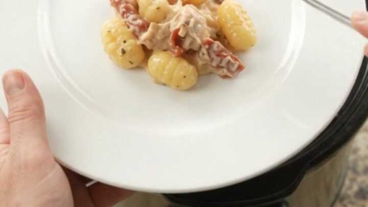 Slow cooker filled with creamy chicken gnocchi topped with melted provolone and ricotta