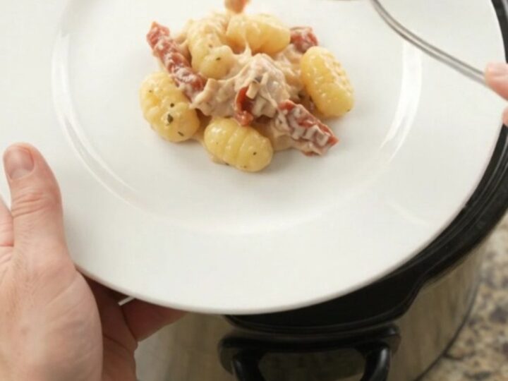 Slow cooker filled with creamy chicken gnocchi topped with melted provolone and ricotta