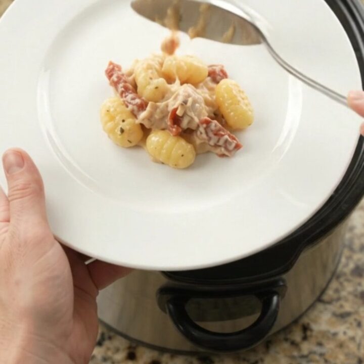 Slow cooker filled with creamy chicken gnocchi topped with melted provolone and ricotta