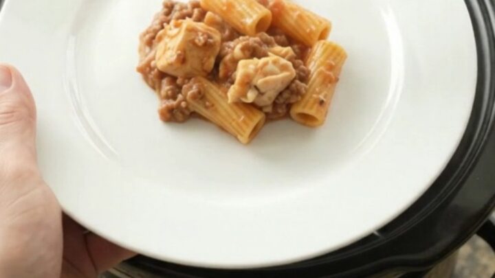 Slow cooker full of creamy chicken rigatoni with melted mozzarella and tomato sauce.