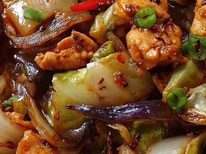 A white bowl filled with glossy, seared chicken and charred cabbage, garnished with fresh chopped scallions.